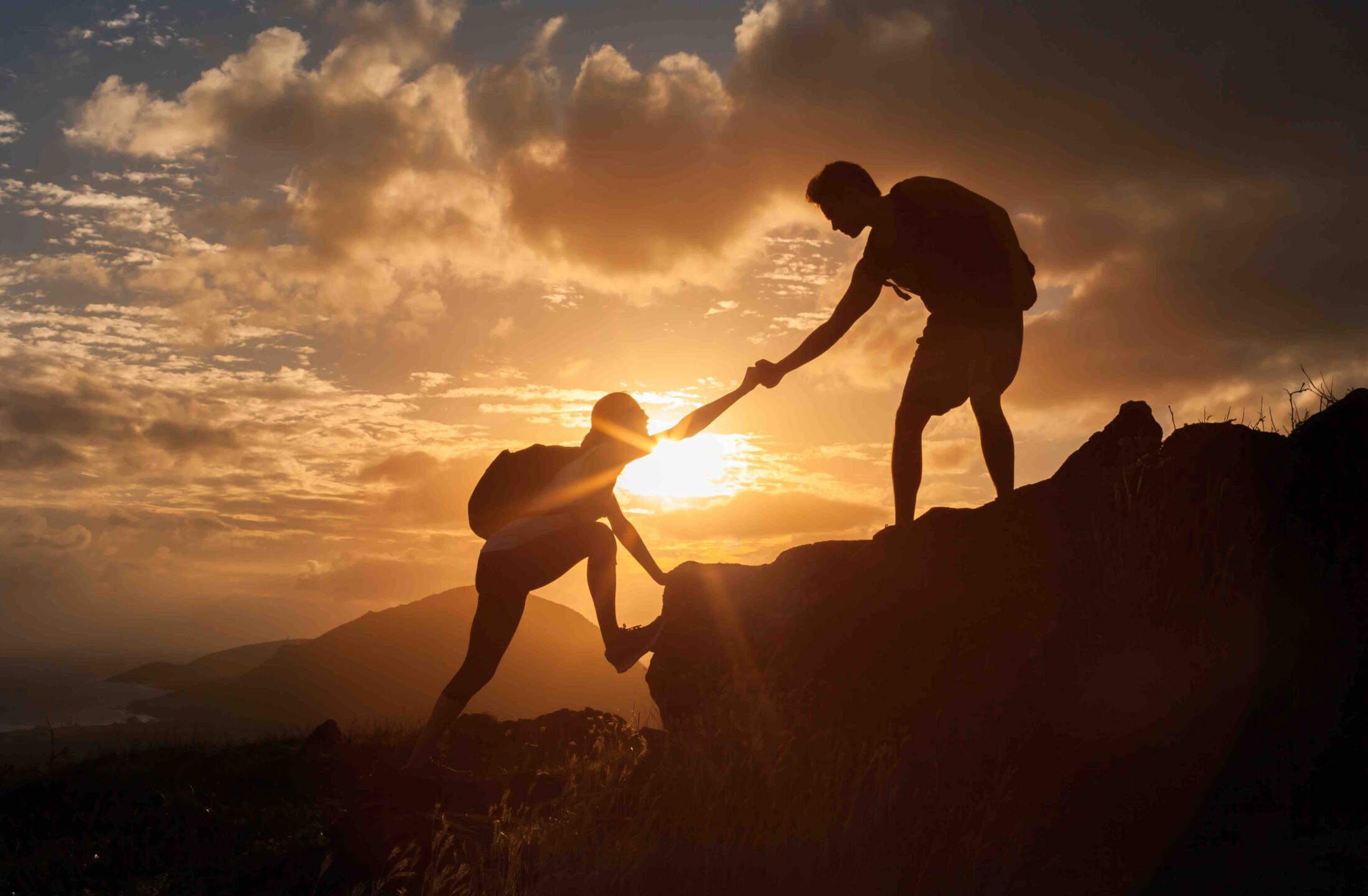 Male and female hikers climbing up mountain cliff and one of them giving helping hand.  People helping and, team work concept.