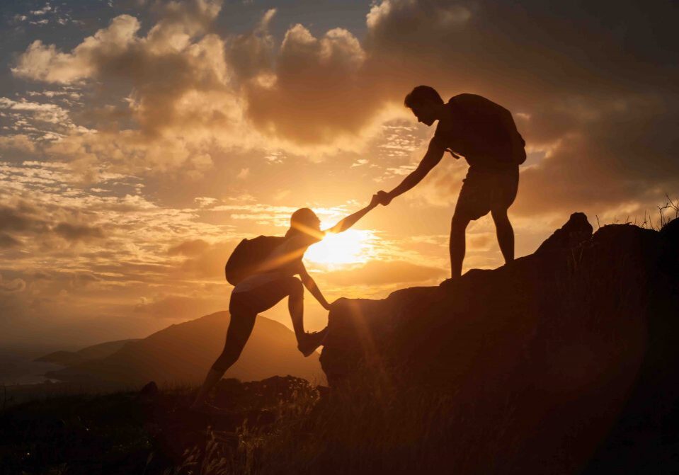 Male and female hikers climbing up mountain cliff and one of them giving helping hand.  People helping and, team work concept.